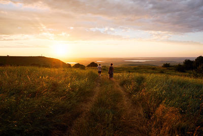 Rear view of man and woman and walking on field against sky during sunset