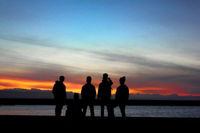 Silhouette people standing on beach against sky during sunset