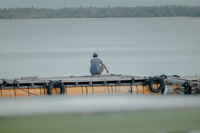 Rear view of man fishing while crouching on pier