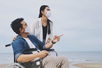 Doctor and patient wearing mask standing at beach against sky