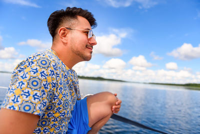 Side view of young man looking away against sky