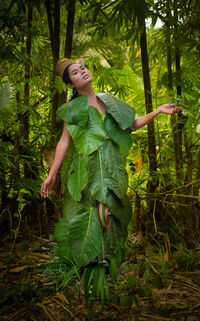 Young woman wrapped in leaves against trees