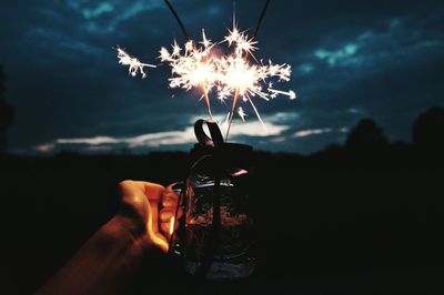 Close-up of hand holding illuminated fire against sky at night