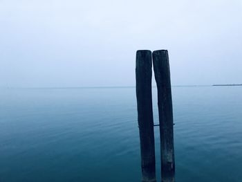 Wooden posts in sea against sky