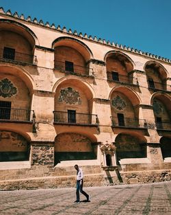 Man walking by historic building against clear sky