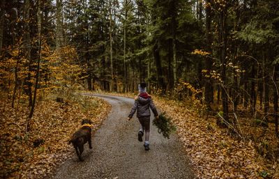 Rear view of girl with dog running on footpath in forest