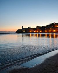 River by illuminated buildings against clear sky at sunset