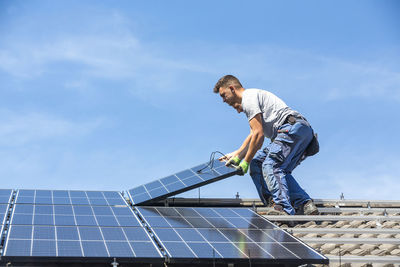 Men holding solar panel while standing on roof against sky