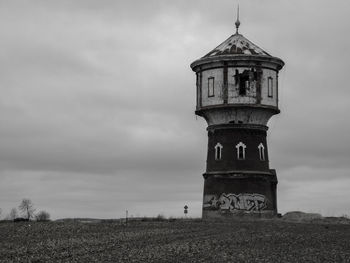 Lighthouse on field by old building against sky