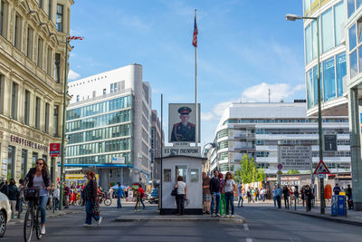 People on city street by buildings against sky