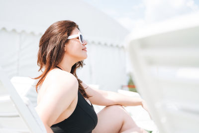 Stylish young woman plus size body positive in black swimsuit and sunglasses rest on beach lounger 