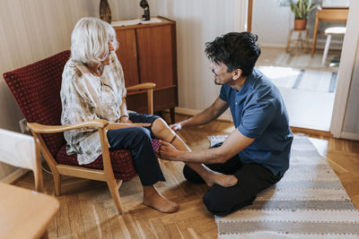 Male care assistant helping senior woman while wearing socks at home