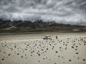 People at desert against cloudy sky