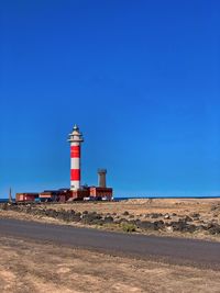 Lighthouse by building against clear blue sky