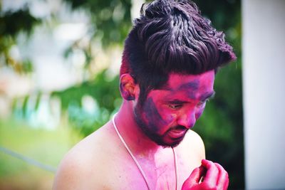 Close-up of shirtless young man with powder paint looking down outdoors