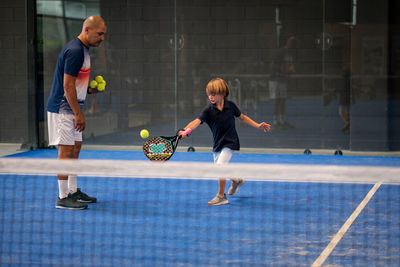 Monitor teaching padel class to child, his student - trainer teaches little boy how to play padel 