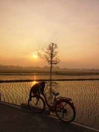 Bicycle by water against sky during sunset