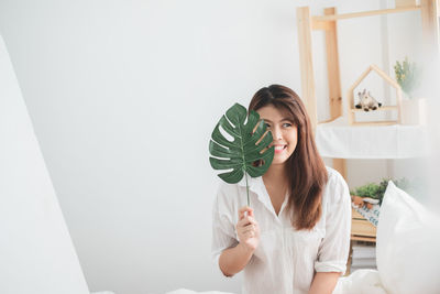 Portrait of smiling young woman holding umbrella against wall