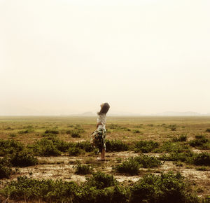 Rear view of man walking on field against clear sky