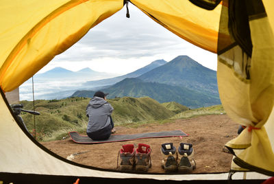 Rear view of men sitting at tent against mountains