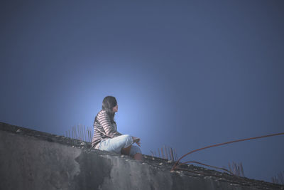 Side view of woman sitting against clear blue sky