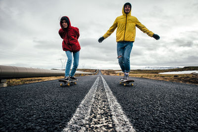Full length of couple skateboarding on road against sky