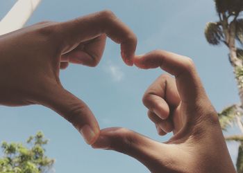 Cropped hands of couple making heart shape against sky