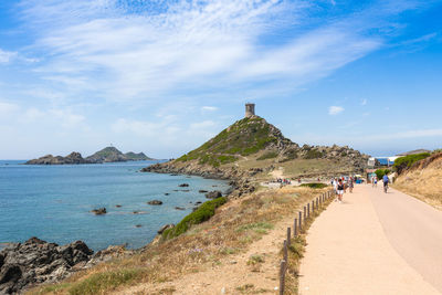 People walking on road by sea against sky