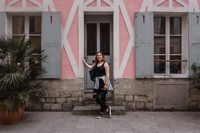 Full length portrait of young woman against building