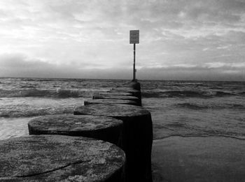 Wooden posts in sea against cloudy sky