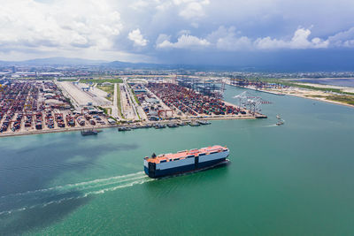 Car carrier sailing on the green sea and international shipping container port background 