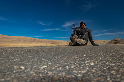 Man sitting on rock in desert against sky
