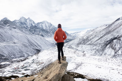 Rear view of tourist standing on rock looking at snow covered landscape