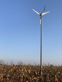 Low angle view of wind turbines on field against clear sky