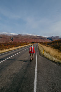 Woman in a red jumper and a scarf walking on the road in iceland