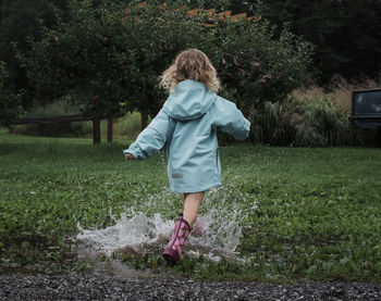 Rear view of playful girl splashing water in puddle at apple orchard