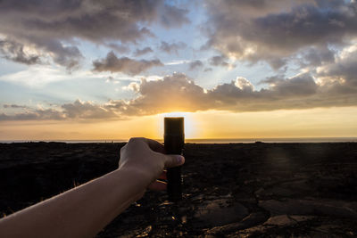 Close-up of person photographing sea against sunset sky