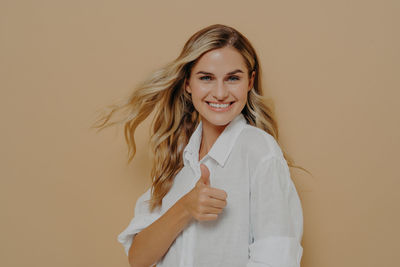 Portrait of smiling young woman standing against pink background