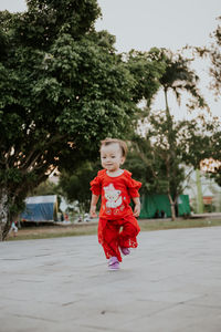 Portrait of cute girl with red umbrella against trees