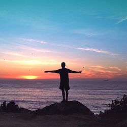 Silhouette of woman standing on beach at sunset