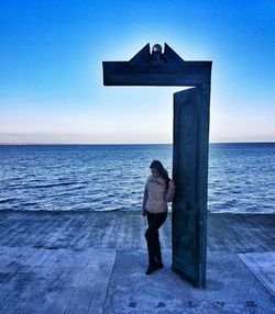 Rear view of woman standing in sea against sky