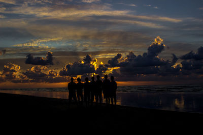 Silhouette people on beach against sky during sunset