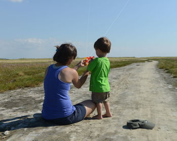 Full length of boy standing on grassy field against cloudy sky learning how to use the kite from his 