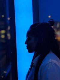 Profile view of young woman looking through window at night