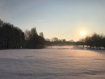 Snow covered landscape against sky during sunset