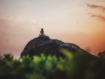 Rear view of woman sitting on rocky mountain against sky during sunset