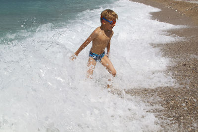 Full length of shirtless boy standing in wave at beach