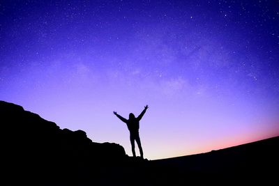 Silhouette of man with arms raised against sky at night