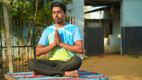 Young fit man wearing sportswear meditating, breathing, sitting with crossed legs in half 