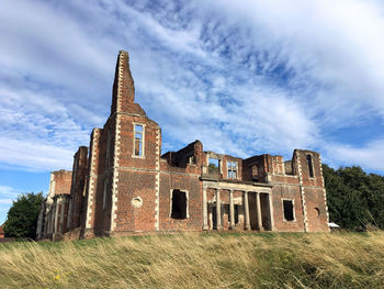 Old ruins of houghton house on grassy field against sky